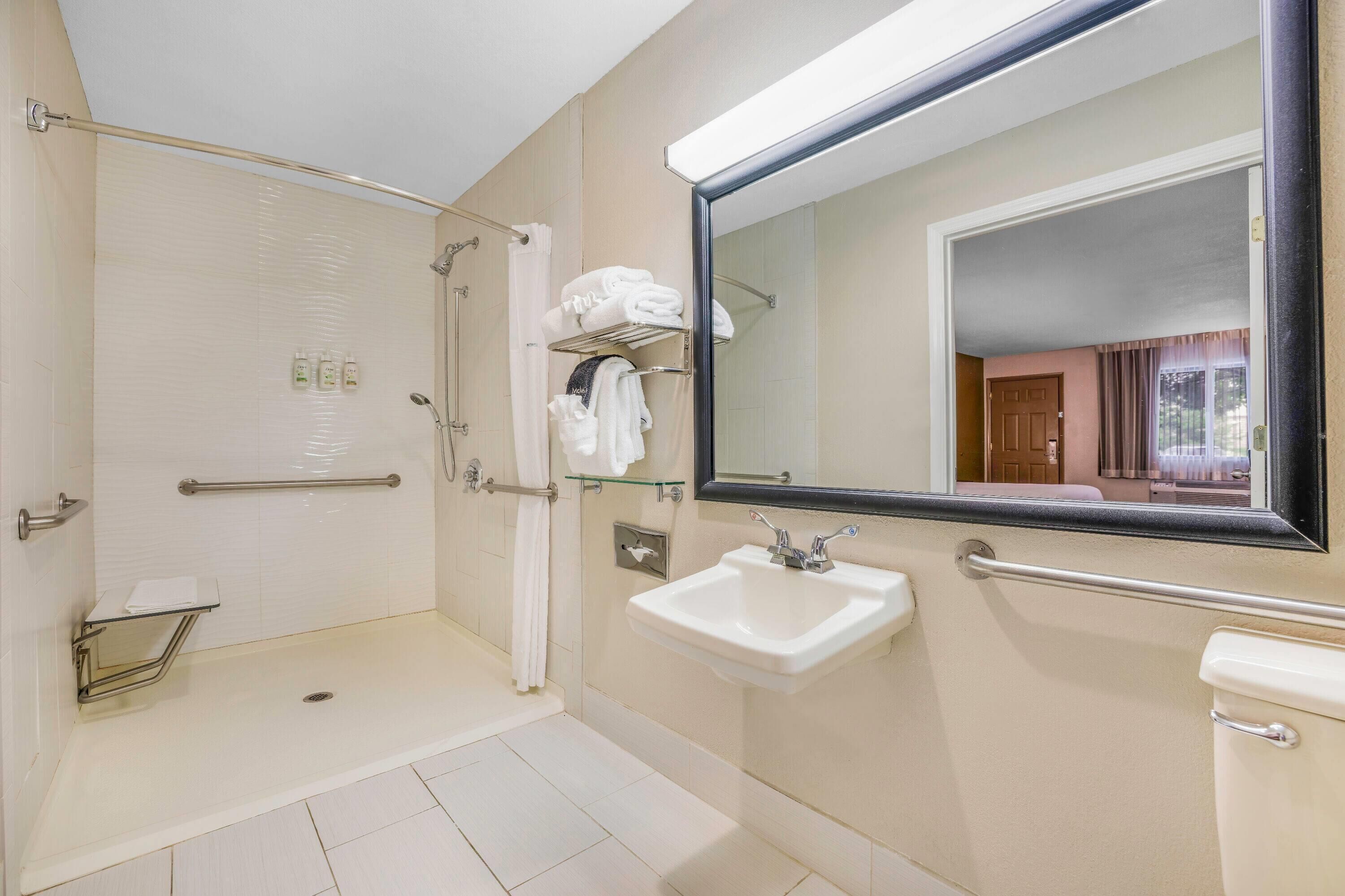 A modern bathroom with a walk-in shower, grab bars, a sink, and a large mirror.