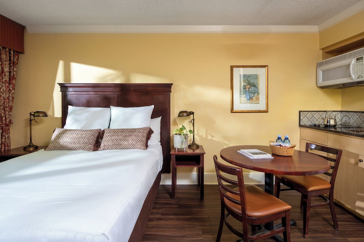 A hotel room with a large bed, a small table with chairs, a microwave, and a framed picture on the wall.