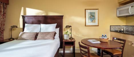 A hotel room with a large bed, a small table with chairs, a microwave, and a framed picture on the wall.