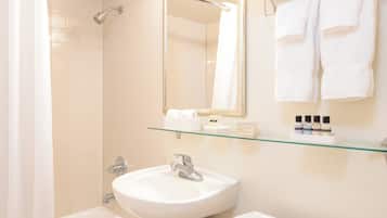 A bathroom with a bathtub, sink, toilet, and a glass shelf with toiletries.