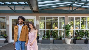 A covered outdoor area with a glass roof, potted plants, and a building entrance. - Park Lane Suites and Inn (Portland)