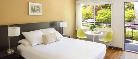 Une chambre d’hôtel avec un grand lit, des lampes de chevet, une petite table avec une chaise, une fenêtre donnant sur l’extérieur et un tableau encadré au mur.