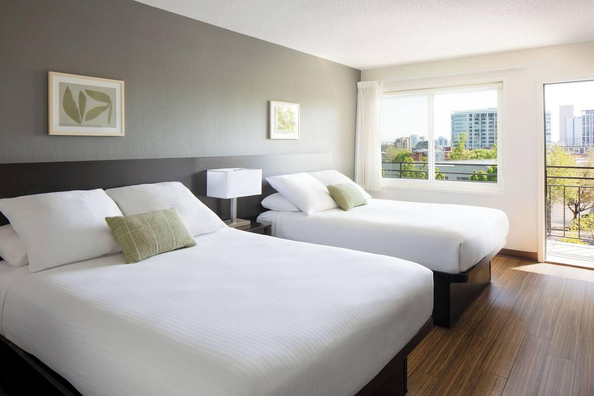 A hotel room with two beds, a city view, and artwork on the walls.