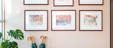 A room with a bench, framed pictures on the wall, a potted plant, and a wicker basket.