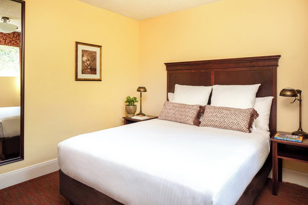 A neatly made bed with white linens, a wooden headboard, and two bedside lamps.