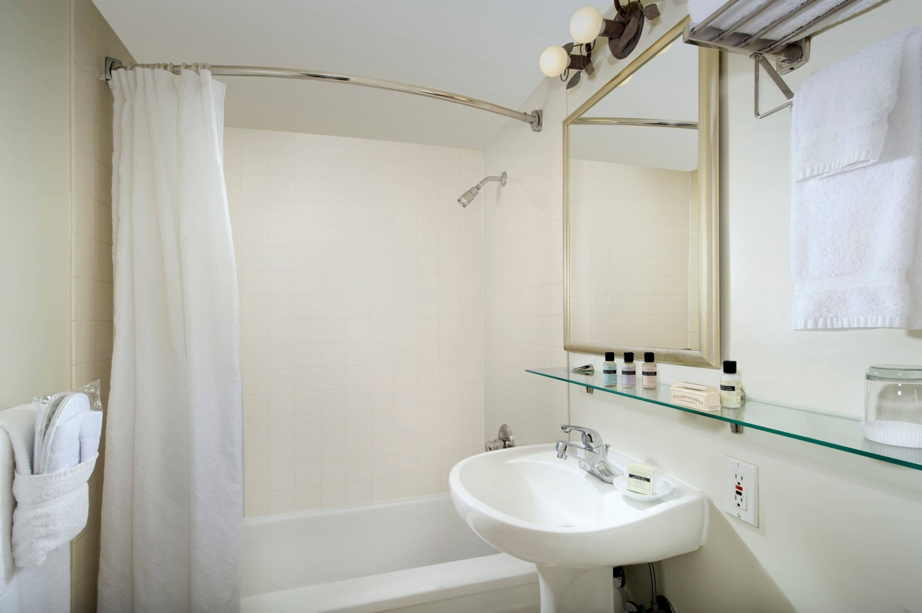 A modern bathroom with a bathtub, a glass shelf with toiletries, and a large mirror.