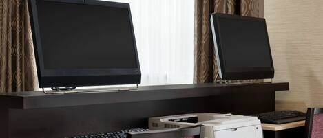 A hotel workspace with two monitors, a keyboard, and a printer on a desk.