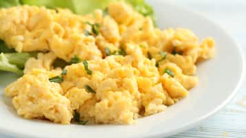 Scrambled eggs on a white plate with chopped herbs, accompanied by a side of green salad.