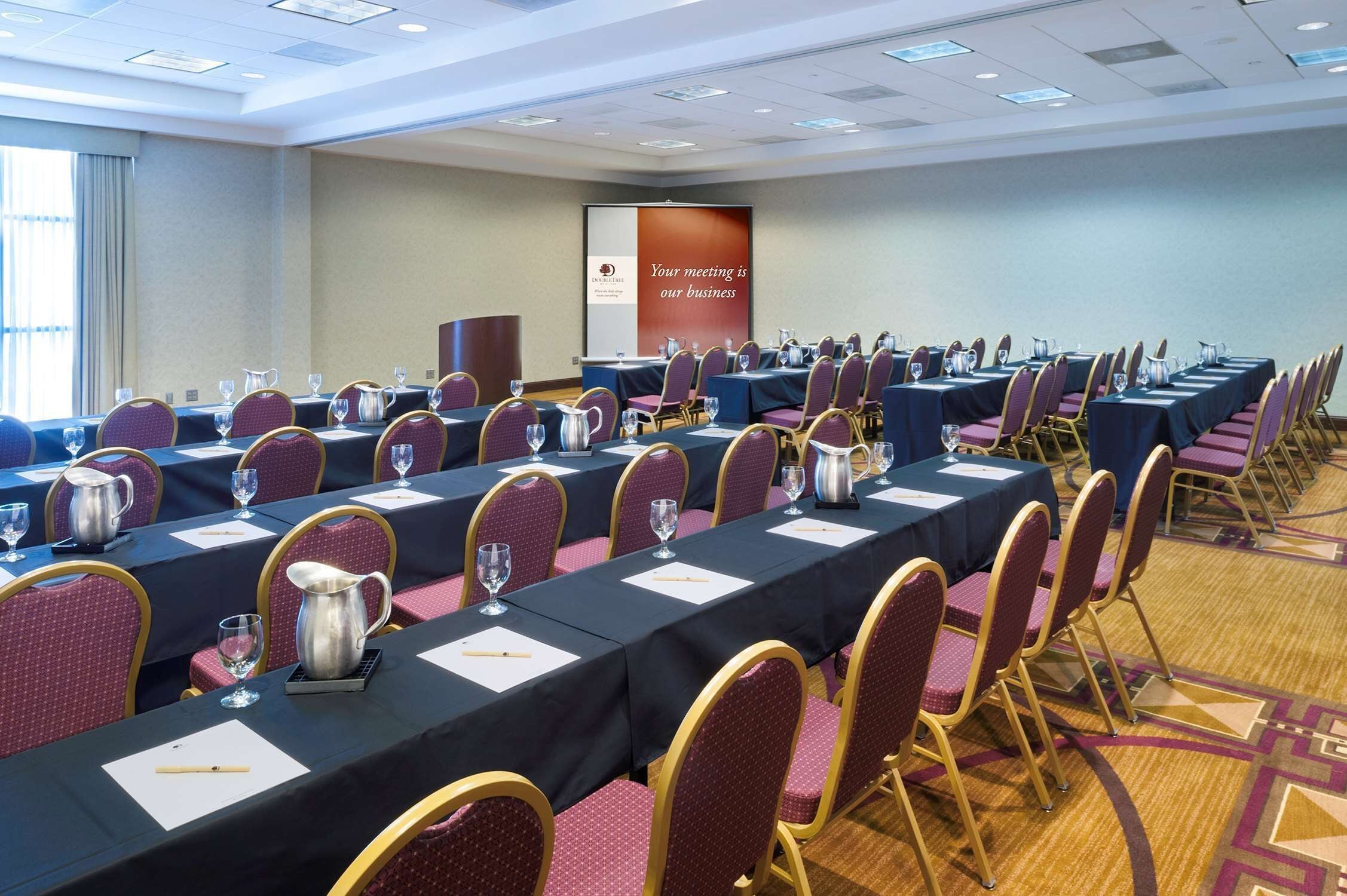 A conference room with rows of tables, chairs, and presentation screens.