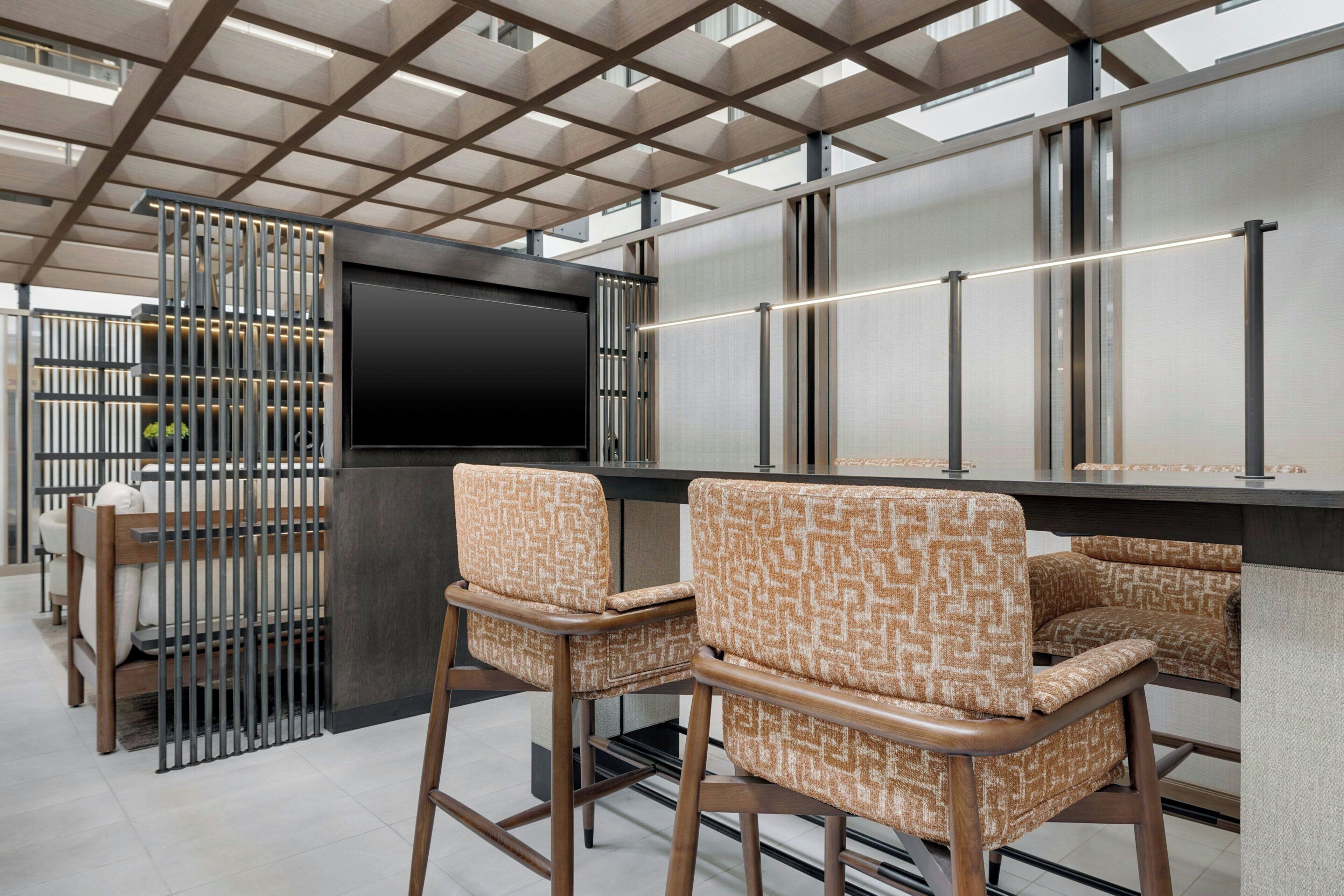 A modern bar area with a flat-screen TV, two patterned bar stools, and a metal grid ceiling.