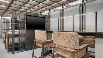 A modern bar area with a flat-screen TV, two patterned bar stools, and a metal grid ceiling.