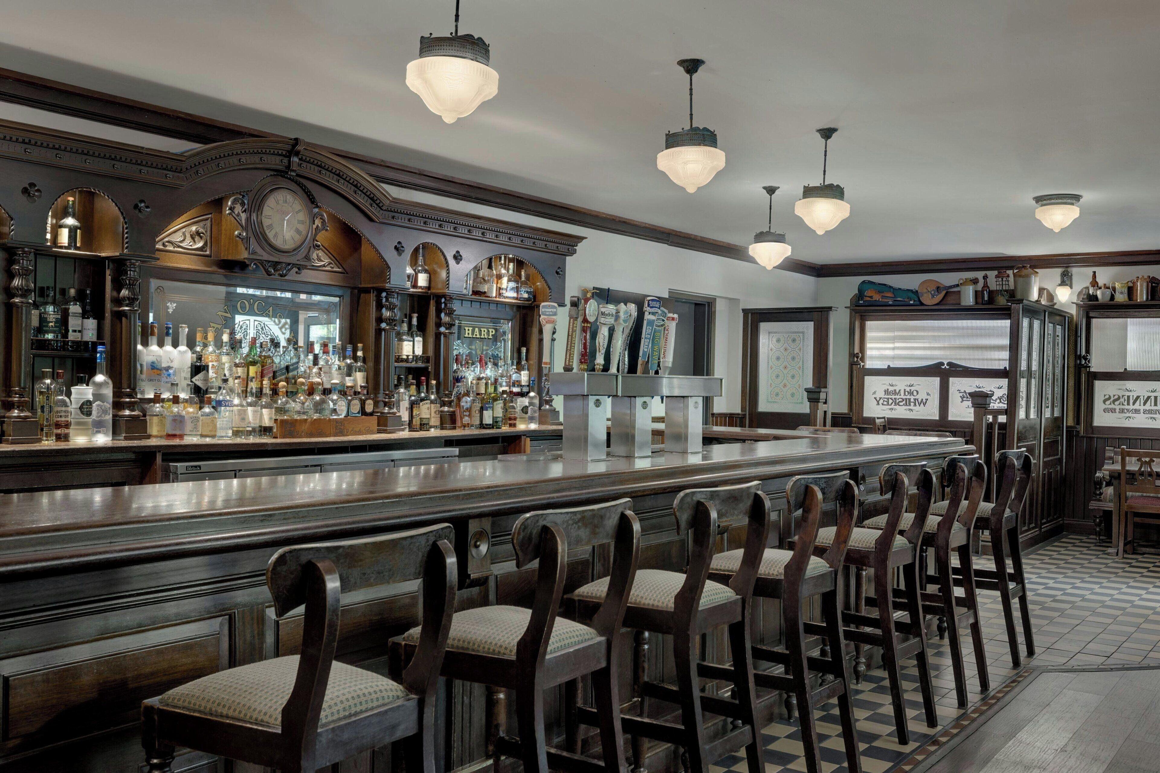 A bar area with a long counter, multiple bar stools, and a variety of bottles and glasses.
