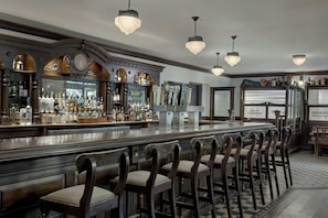 Una zona de bar con una barra alargada, varios taburetes y una amplia variedad de botellas y vasos.