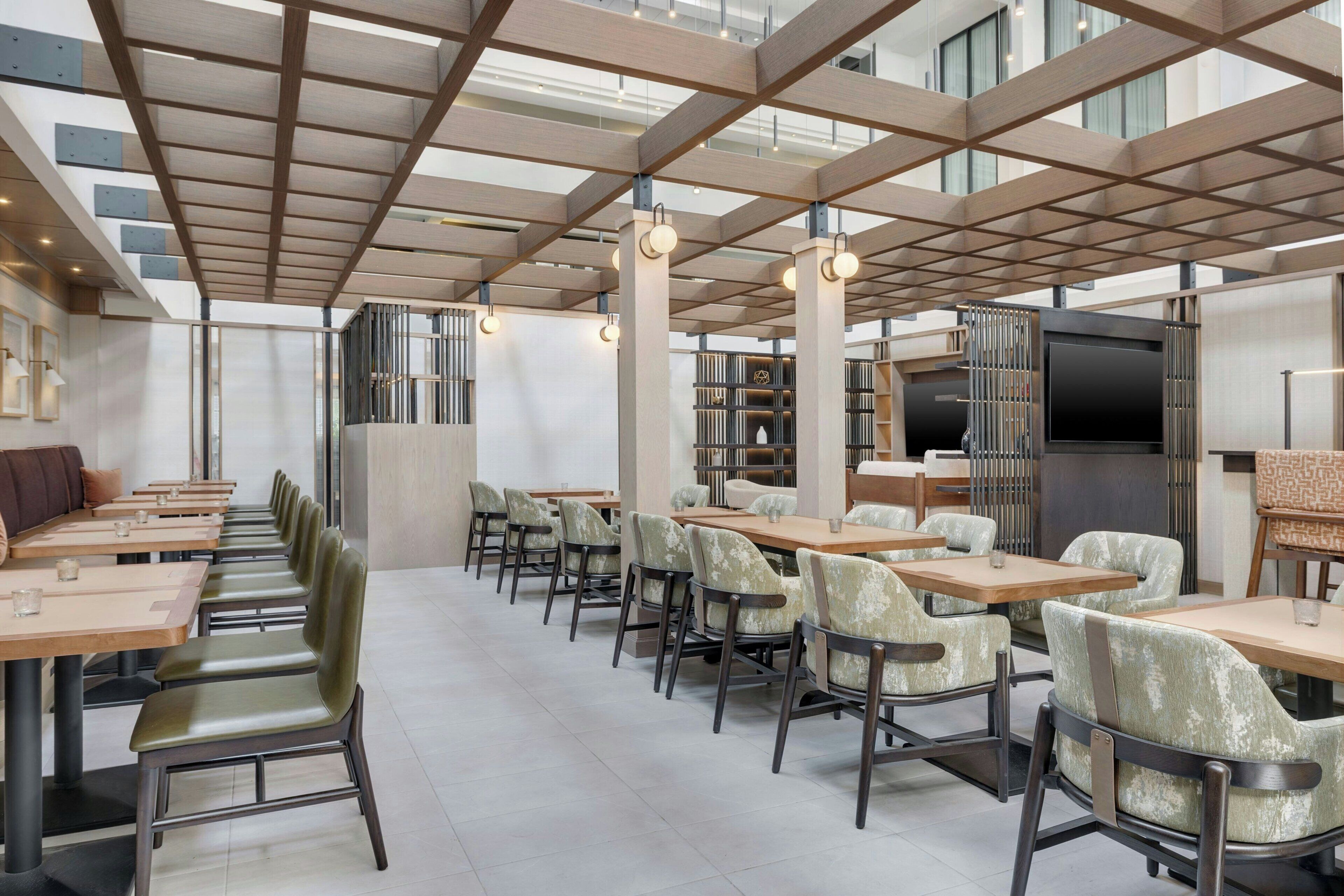 A modern restaurant with a high ceiling, exposed beams, and a mix of seating options including tables and chairs.