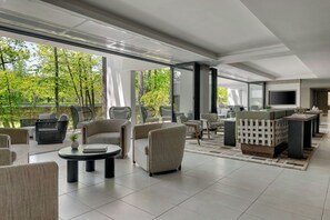 Ein modernes Wohnzimmer mit großem Fernseher, bequemen Sitzmöglichkeiten und Blick auf Bäume.