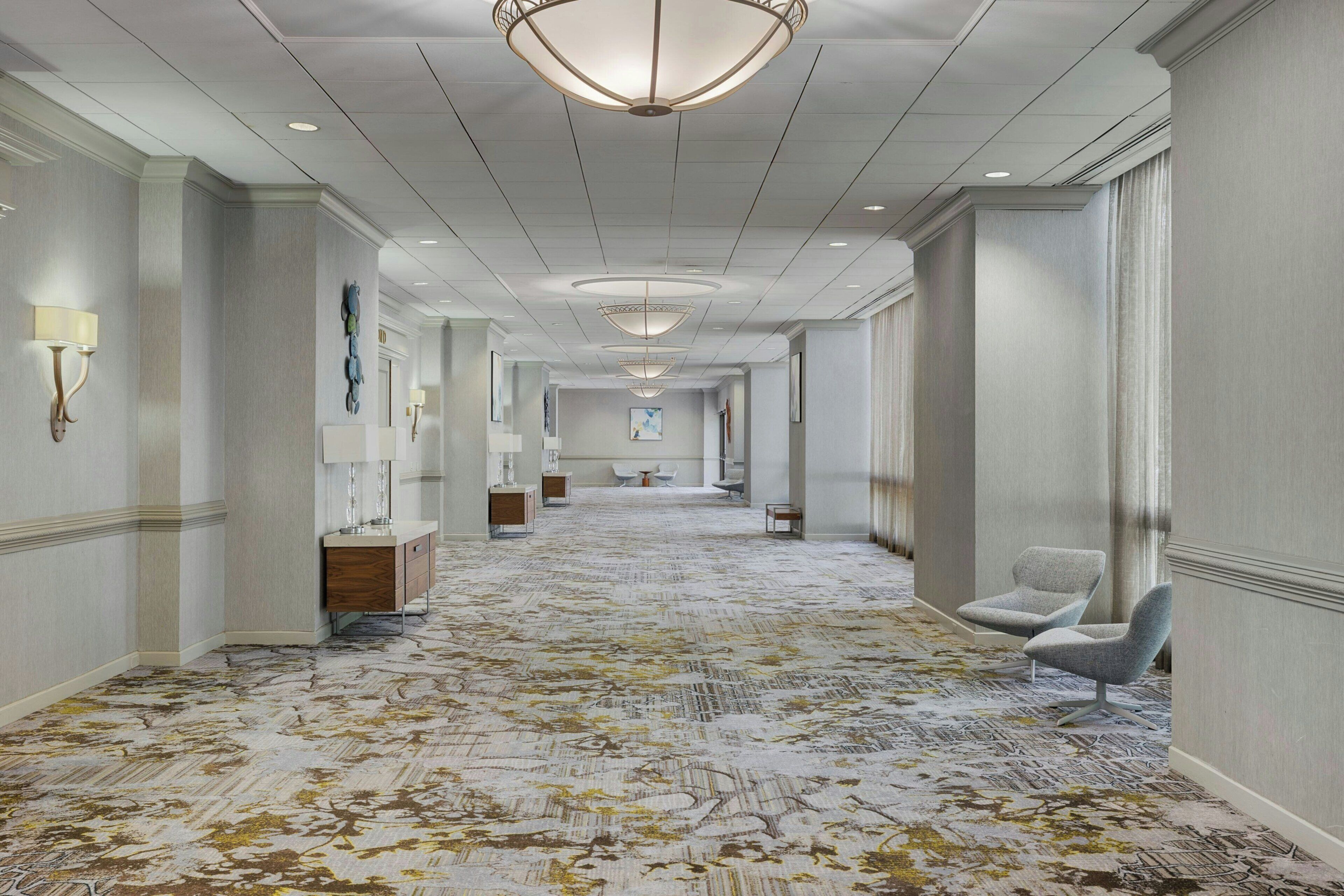 Un pasillo de hotel con alfombra estampada, apliques en la pared y un candelabro.