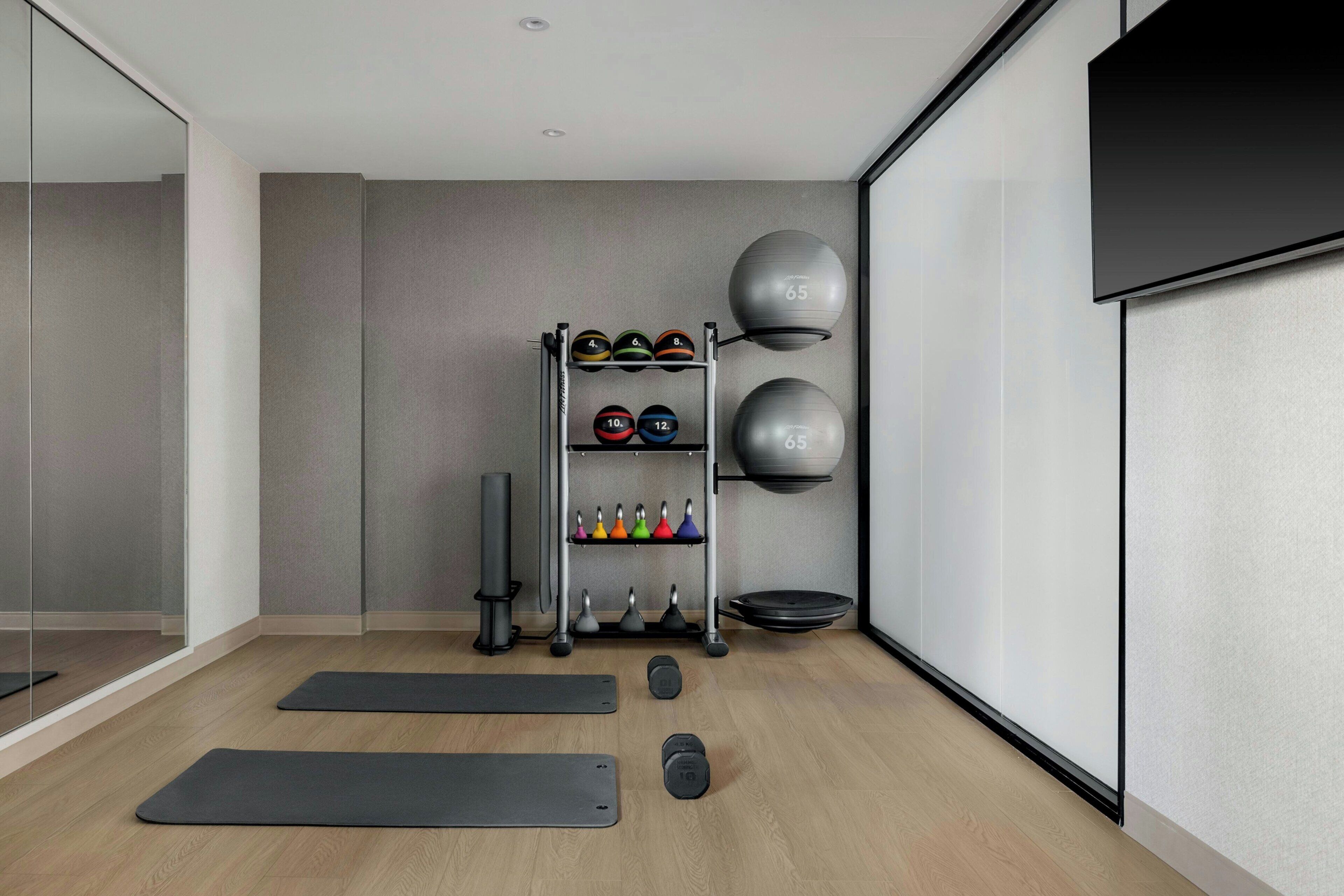 A modern gym with exercise equipment, yoga mats, and a mirrored wall.