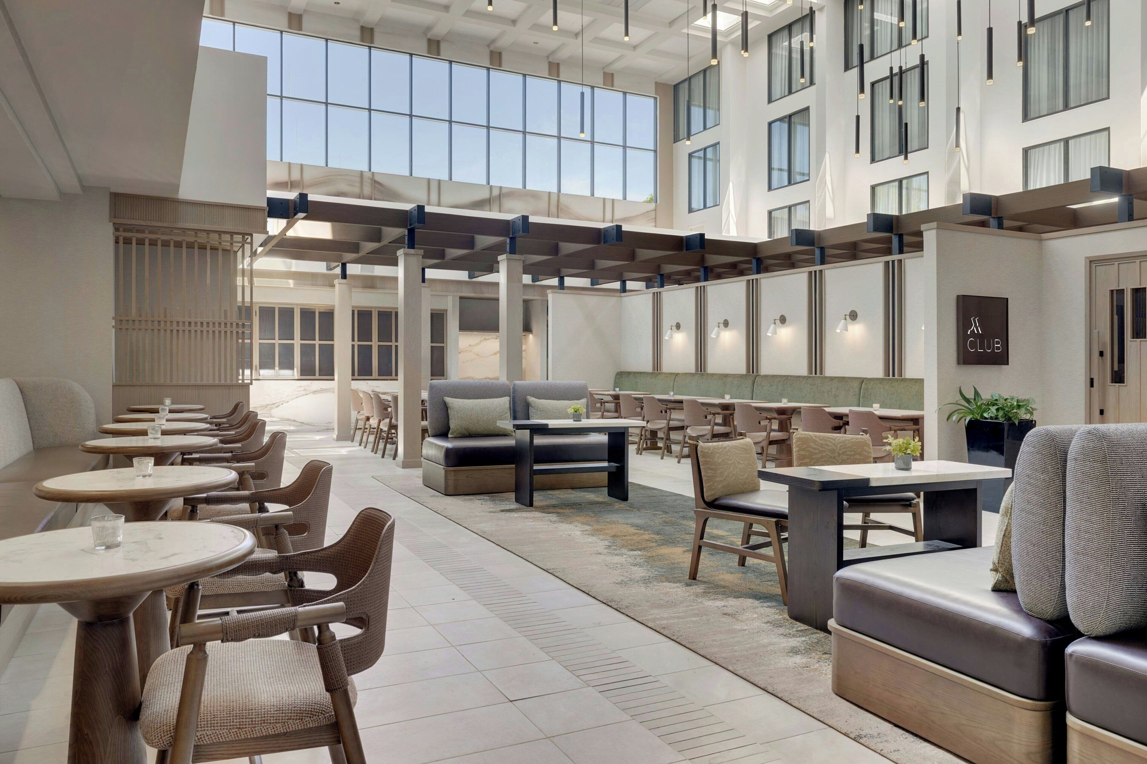 A spacious indoor area with multiple seating options including tables and sofas, a central coffee table, and a large window providing natural light.