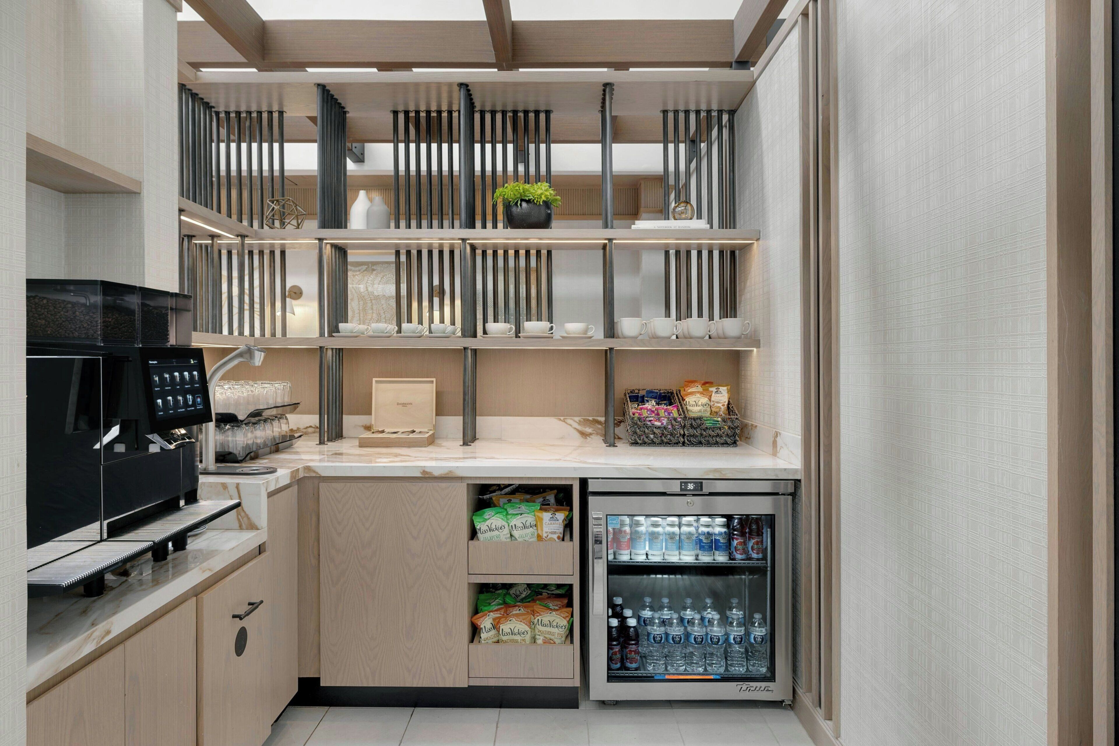 Een compacte keuken met een koffieapparaat, een gevulde koelkast en een klein kastje met snacks.