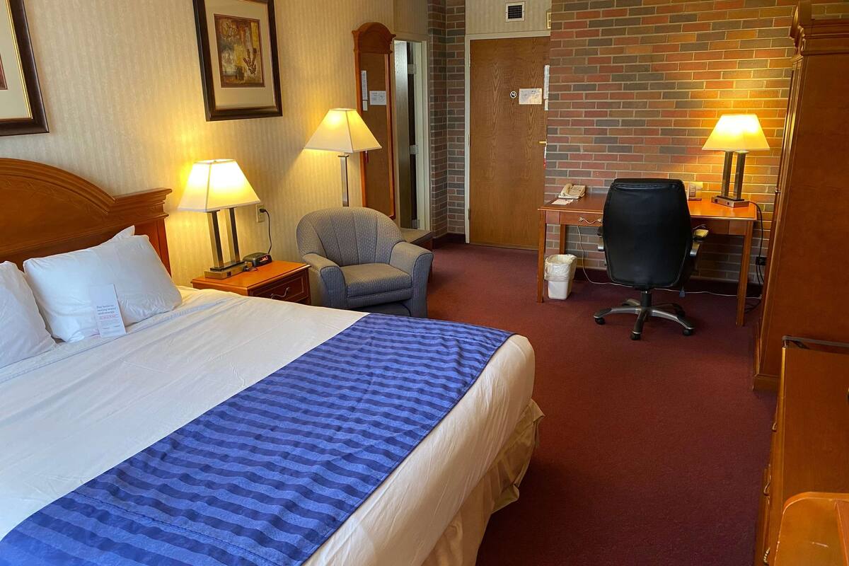 Una habitación de hotel con una cama grande, dos sillas, un escritorio y dos lámparas.