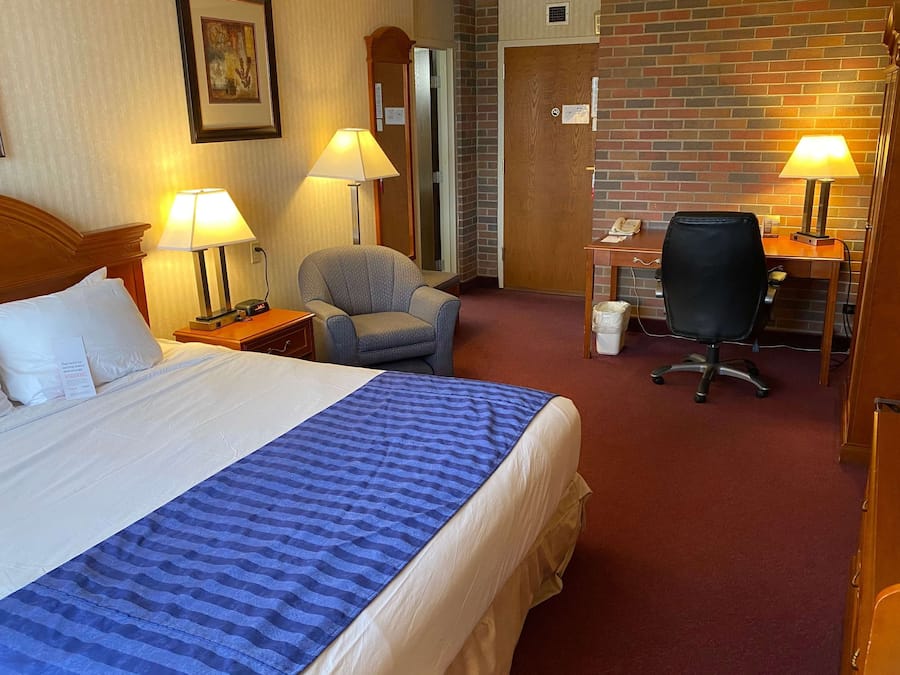 Une chambre d’hôtel avec un grand lit, deux fauteuils, un bureau et deux lampes.