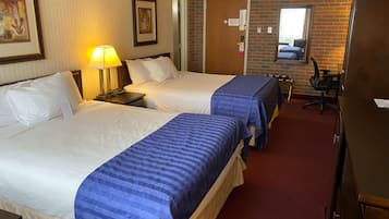 Una habitación de hotel con dos camas, un escritorio, una silla, una lámpara y un espejo.