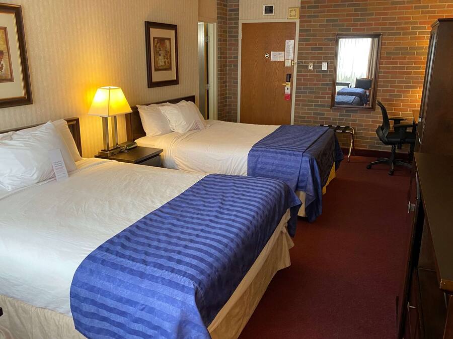 Una habitación de hotel con dos camas, un escritorio, una silla, una lámpara y un espejo.