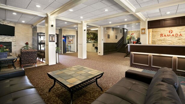 A spacious lobby with a reception desk, seating area, and a staircase leading to an upper floor. - Ramada by Wyndham Lethbridge (Lethbridge)