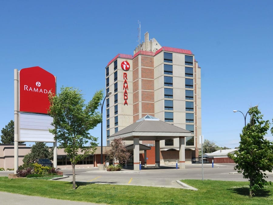 Un hotel Ramada amb un cartell vermell ben visible, entrada coberta i un aparcament.