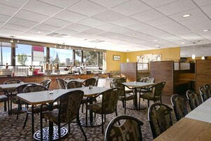 A restaurant with multiple tables and chairs, a kitchen area, and large windows providing a view of the outdoors.