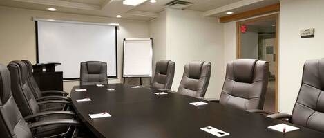 A conference room with a long table, six chairs, a projector screen, and a whiteboard.