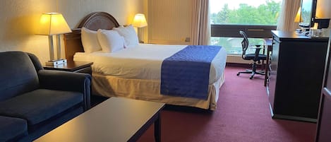 A hotel room with a bed, two bedside lamps, a desk with a chair, a television, and a window with a view of trees.