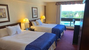 A hotel room with two beds, a desk, a chair, and a view of a green landscape. - Ramada by Wyndham Lethbridge (Lethbridge)