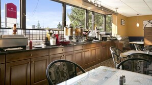 A kitchen with a large window, wooden cabinets, and a dining area with chairs and a table. - Ramada by Wyndham Lethbridge (Lethbridge)