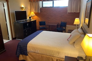 A hotel room with a bed, a desk, two chairs, a television, and a window with curtains.