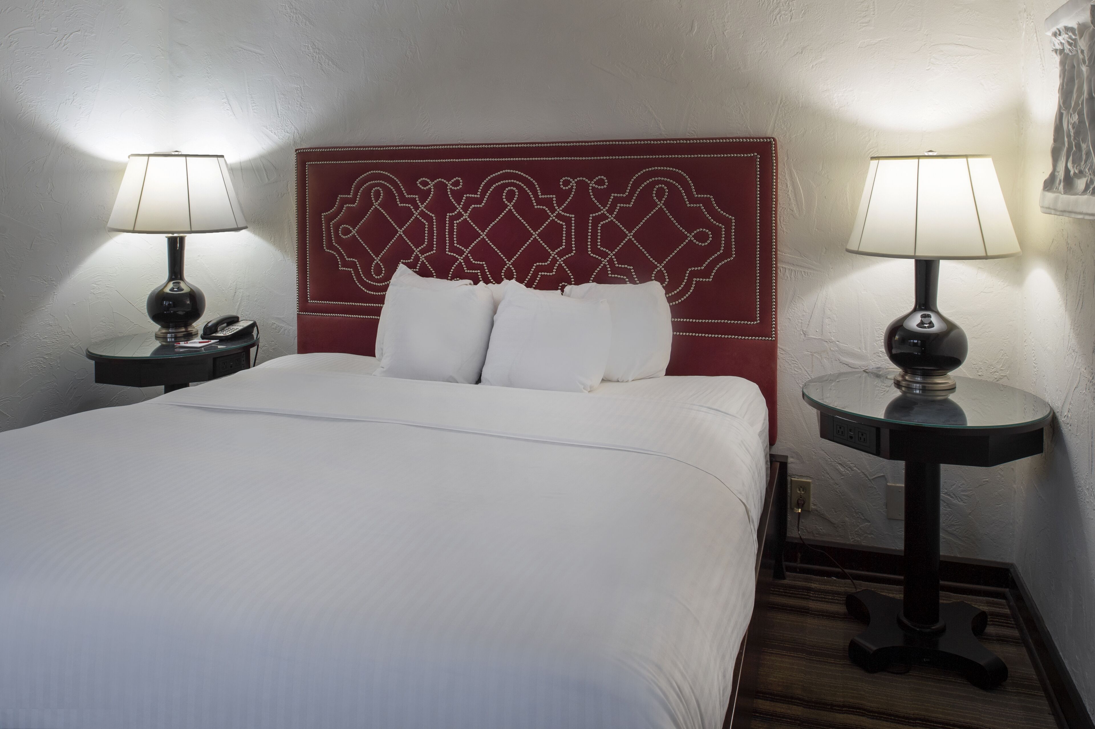 A hotel room with a large bed, two bedside tables with lamps, and a decorative headboard.