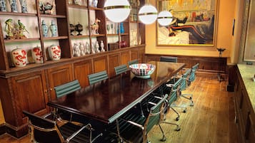 Un salón de conferencias con una larga mesa de madera, sillas tapizadas en verde y un jarrón grande sobre la mesa.