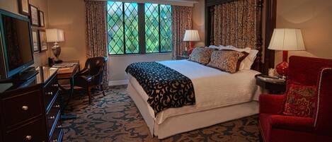 A hotel room with a large bed, two bedside lamps, a desk with a chair, a television, and a window with curtains.