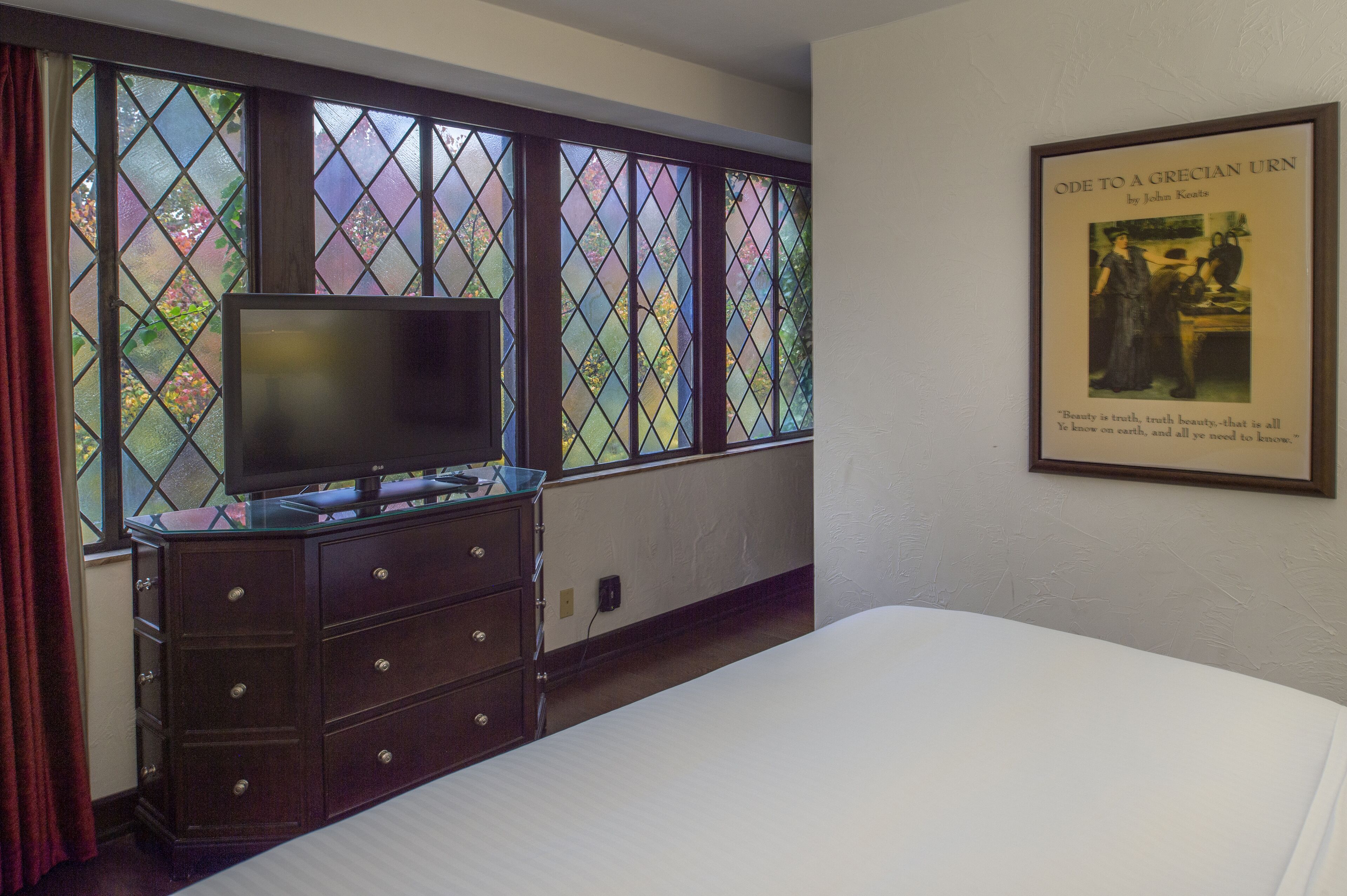 A hotel room with a large window, a dresser, a bed, and a framed picture on the wall.