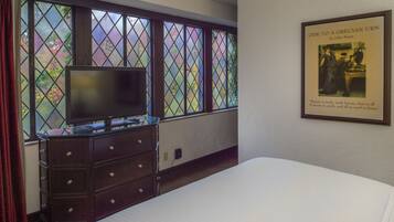A hotel room with a large window, a dresser, a bed, and a framed picture on the wall.
