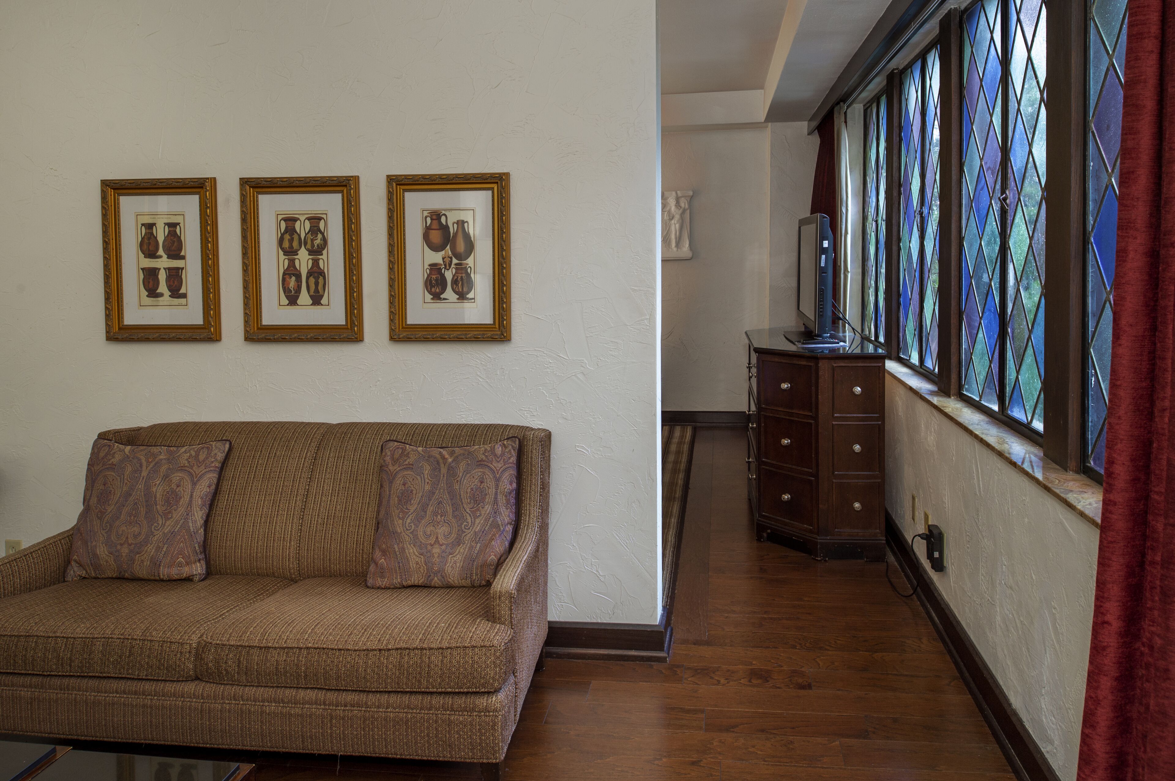 A living room with a brown sofa, three framed pictures on the wall, and a wooden cabinet.