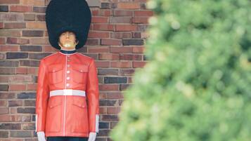 A statue of a guard in a red uniform with a tall black hat, standing against a brick wall.