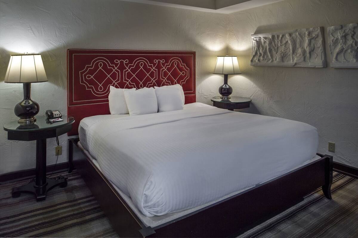 A hotel room with a large bed, two bedside tables with lamps, a red headboard, and wall art.