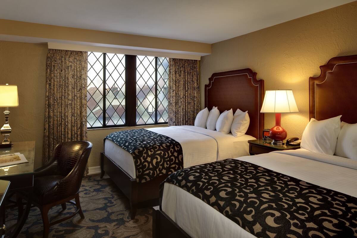 A hotel room with two beds, a desk, a chair, and a window with curtains.