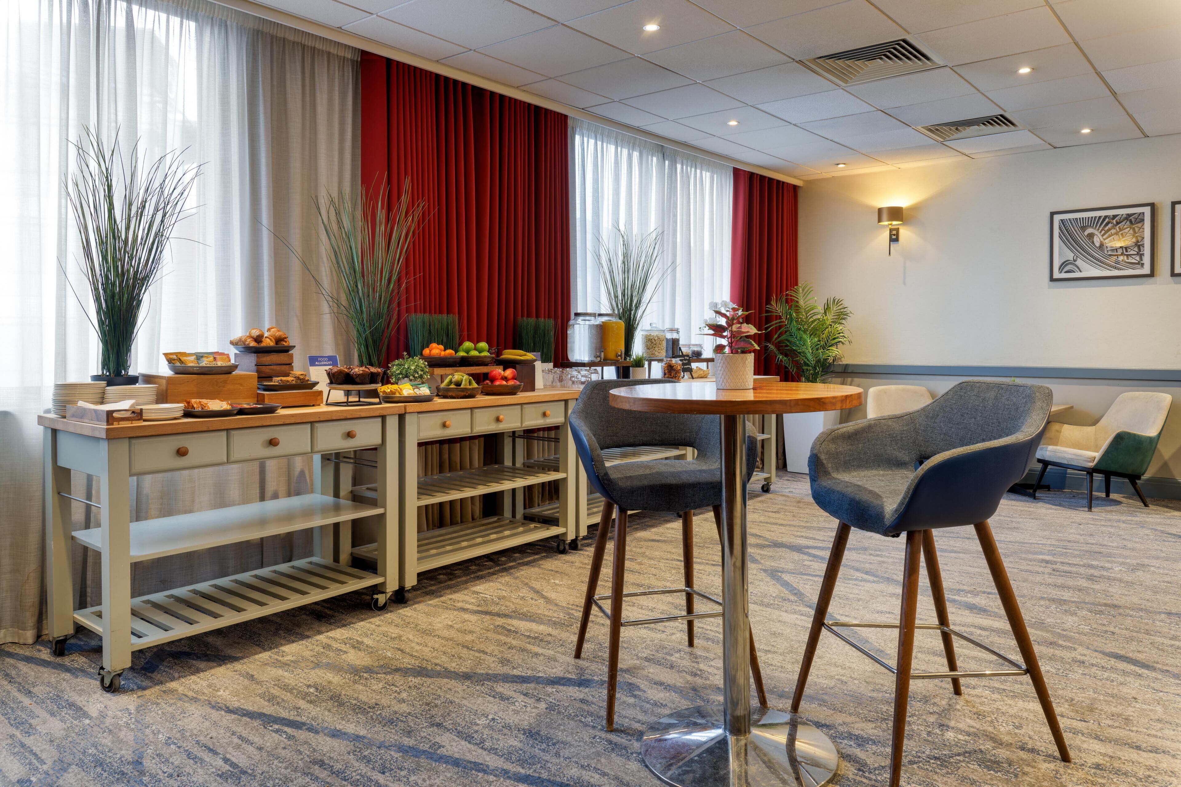 A hotel room with a dining area featuring a buffet table, two bar stools, a small round table, and a sofa.
