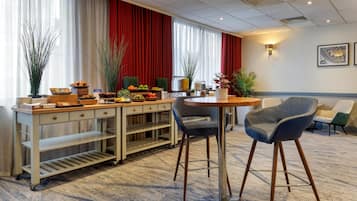 A hotel room with a dining area featuring a buffet table, two bar stools, a small round table, and a sofa.