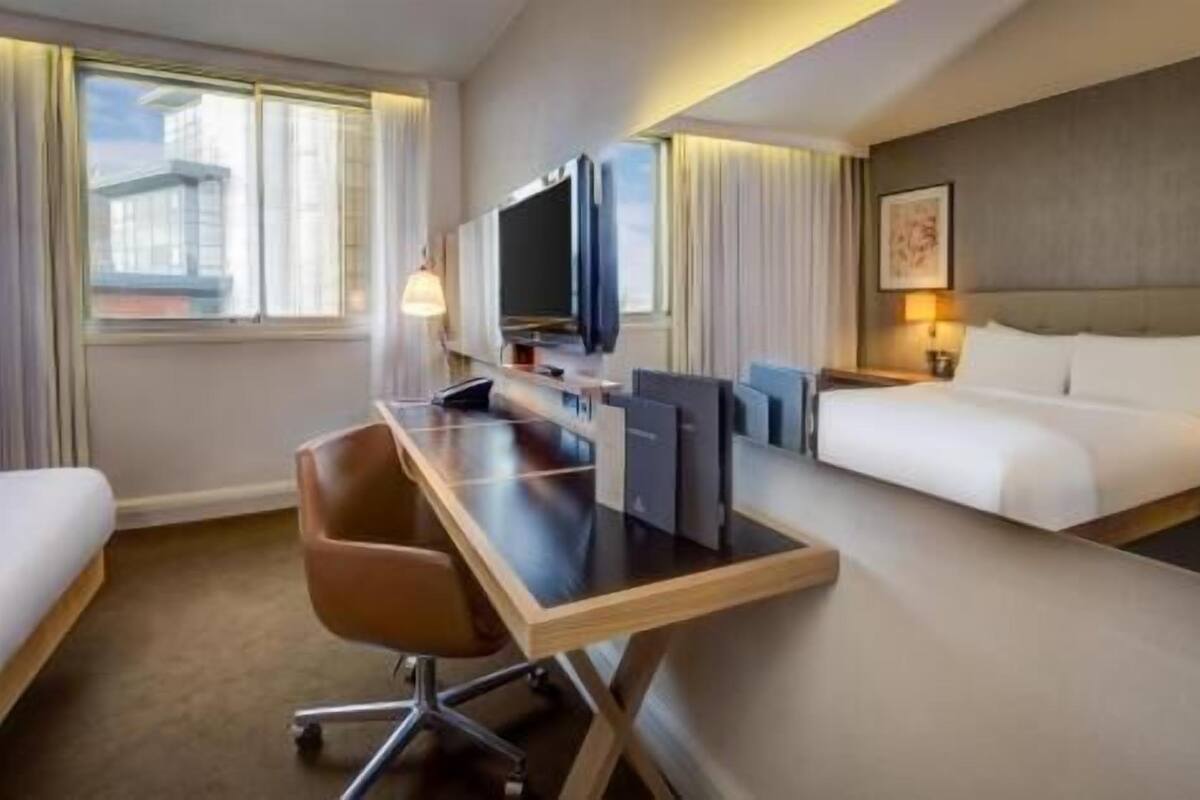 A hotel room with a bed, a desk with a chair, a television, and a window.