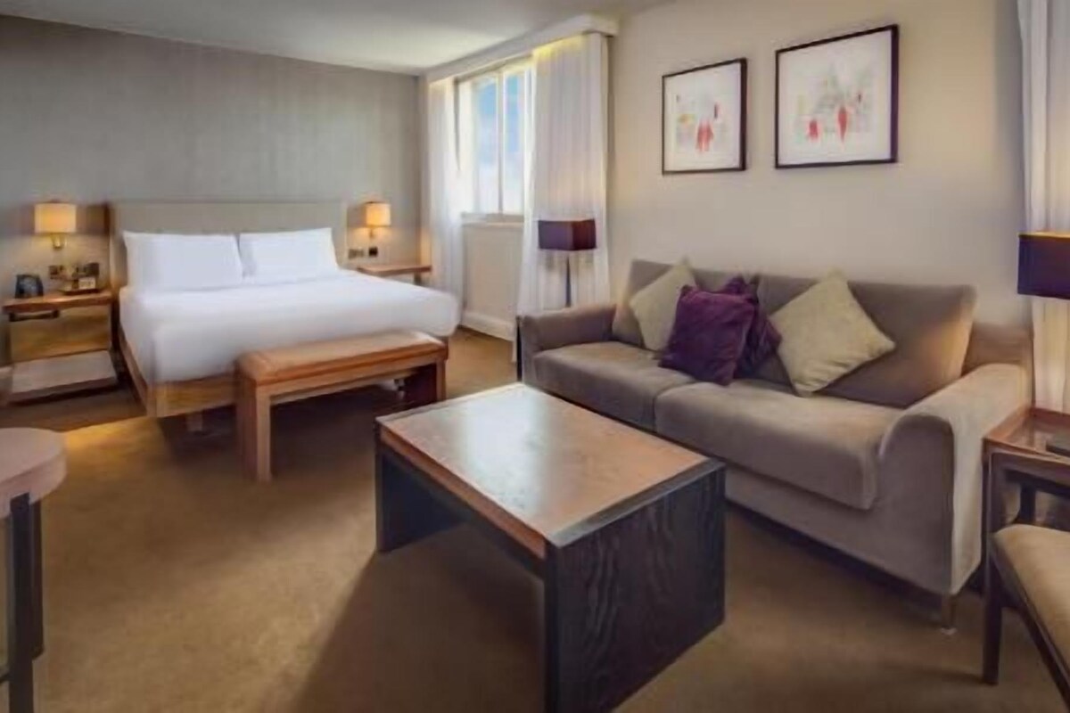 A hotel room with a bed, a sofa, a coffee table, and two lamps.