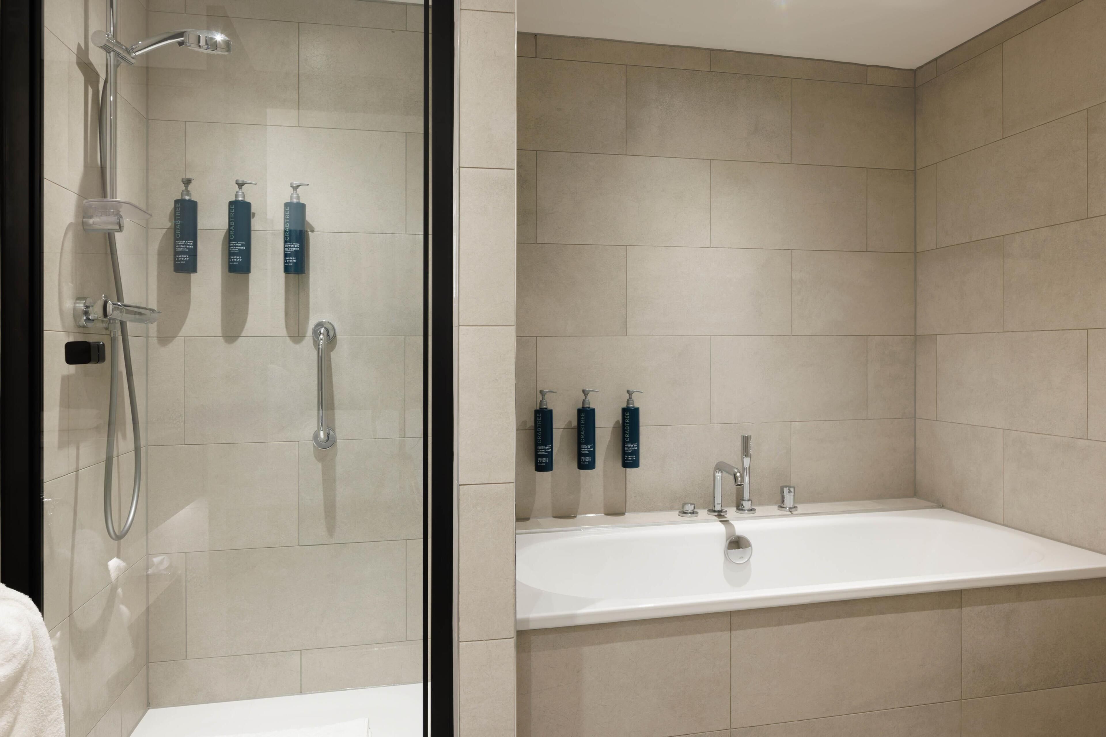 A modern bathroom with a shower, a bathtub, and three bottles of shampoo on the wall.