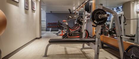 A gym with weightlifting equipment, a bench, and a mirror reflecting the space.